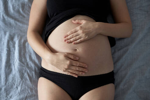 Pregnant woman touching stomach while lying on bed at home - BZF00587