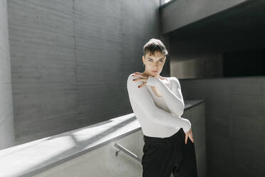 Trans young man wearing white leotard posing while standing in basement - TCEF01122