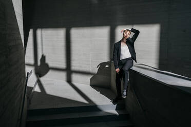 Sunlight falling on trans young man sitting on retaining wall in basement - TCEF01125