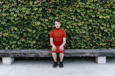 Gender fluid man sitting on bench in public park - TCEF01136