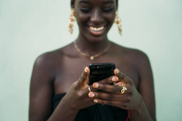 Young woman using mobile phone while standing against green wall - MPPF01096