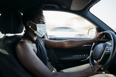 Junge Frau mit Gesichtsmaske, die sich auf das Autofahren konzentriert - MPPF01100