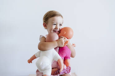 Baby girl embracing toys while sitting against wall - EBBF00767