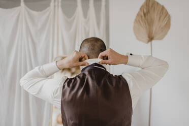 Bridegroom tying bow while standing at wedding dress shop - SMSF00319