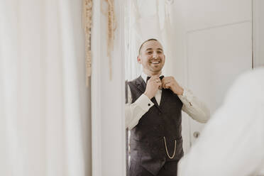 Bridegroom adjusting bow while looking in mirror at wedding dress shop - SMSF00330