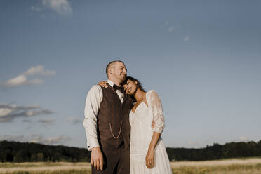 Bride leaning on bridegroom's shoulder while standing at field - SMSF00337