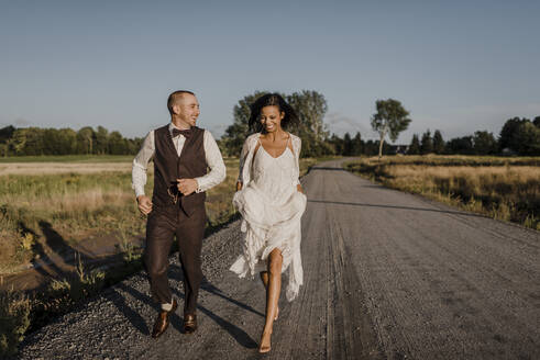 Glückliche Braut und Bräutigam laufen auf der Straße an einem sonnigen Tag - SMSF00340