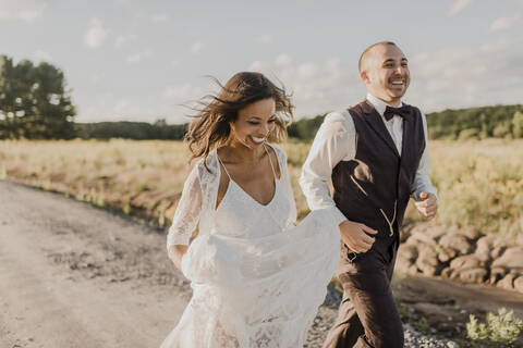 Happy heterosexual couple running on road during sunny day stock photo