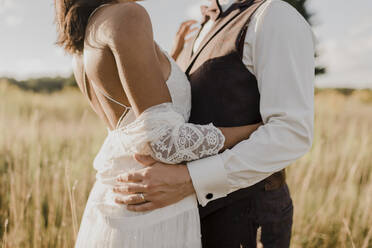 Midsection of couple embracing each other at field on sunny day - SMSF00342