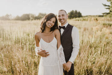 Smiling couple standing against agricultural field on sunny day - SMSF00345