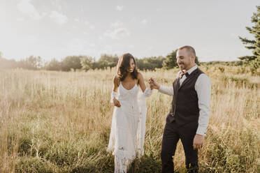 Paar hält sich an der Hand und geht in einem Feld an einem sonnigen Tag - SMSF00346