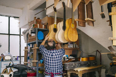 Älterer Mann hängt Gitarre in einer Reihe in der Werkstatt auf - DGOF01459