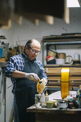 Luthier polishing guitar while standing by workbench at workshop - DGOF01463