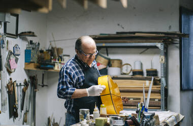 Man polishing guitar while standing by workbench at workshop - DGOF01465