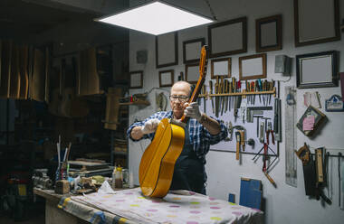 Mann hält Gitarre auf Werkbank bei der Arbeit in der Werkstatt - DGOF01467