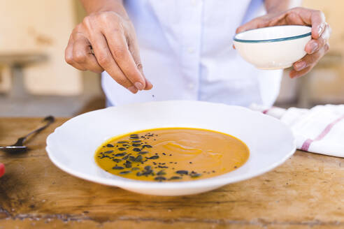 Frau gibt Sesamsamen in die Suppe, während sie am Tisch steht - FMOF01073