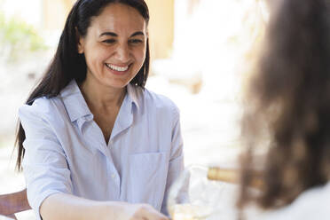 Woman serving wine to friend while sitting at back yard - FMOF01083
