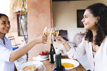 Freunde stoßen mit Weingläsern an, während sie am Esstisch im Hinterhof sitzen - FMOF01090