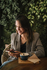 Junge Frau, die in einem Café sitzt und mit ihrem Smartphone SMS schreibt - GRCF00367
