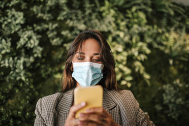 Woman using smart phone wearing protective face mask while sitting in cafe - GRCF00369