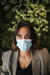 Young woman wearing protective face mask sitting in cafe - GRCF00370