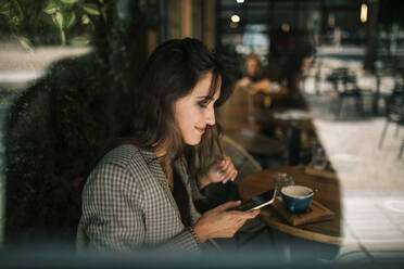 Smiling young woman text messaging on smart sitting in cafe - GRCF00371