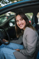 Lächelnde junge Frau, die im Auto sitzend nach draußen schaut - GRCF00383