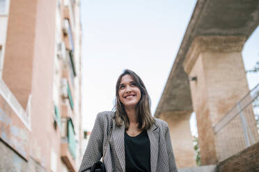 Smiling young woman standing against building exterior in city - GRCF00384