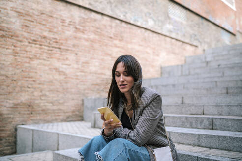 Frau benutzt Mobiltelefon, während sie auf einer Treppe sitzt - GRCF00387