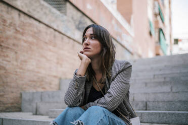 Thoughtful woman with hand on chin sitting outdoors - GRCF00389