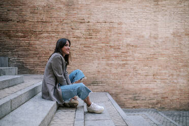 Smiling young woman sitting on staircase - GRCF00390