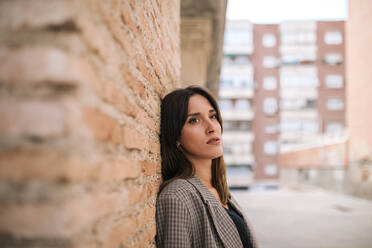 Young woman looking away while standing against brick wall - GRCF00393