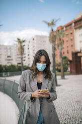 Young woman text messaging on smart phone while standing in city - GRCF00395