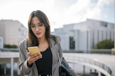 Woman using smart phone while standing in city - GRCF00397