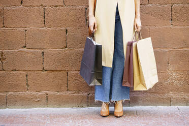 Woman carrying shopping bag while standing against brick wall - JSMF01720