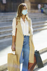 Woman with face mask carrying bag while walking on staircase in city - JSMF01725