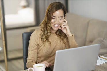 Businesswoman smiling while working on laptop at home - JSMF01737