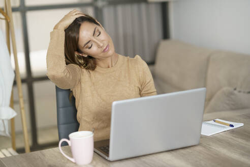 Geschäftsfrau macht Nackenübung bei der Arbeit am Laptop zu Hause - JSMF01740
