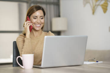 Businesswoman smiling while talking on phone at home - JSMF01742