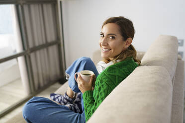 Woman drinking coffee while sitting on sofa at home - JSMF01746