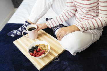 Frau sitzt mit Frühstück und Kaffee auf dem Bett zu Hause - JSMF01751