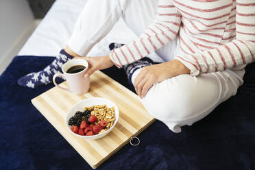 Woman sitting with breakfast and coffee on bed at home - JSMF01751