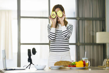 Frau versteckt Gesicht mit Obst während Online-Tutorial zu Hause - JSMF01762