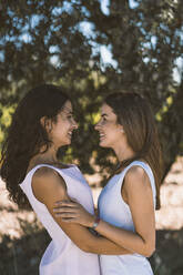 Smiling lesbian couple embracing each other while standing against tree - DAMF00471