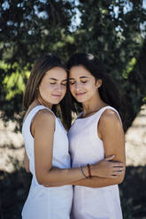 Lesbian couple with eyes closed standing against tree - DAMF00473