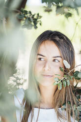 Young woman looking away while standing under tree - DAMF00481