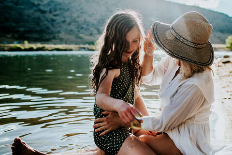 Mother and daughter sitting on lake shore having a quiet moment stock photo