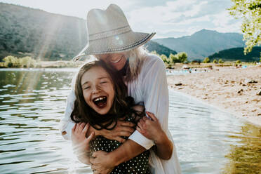 Mom and daughter hugging and laughing while standing in a lake - CAVF89495