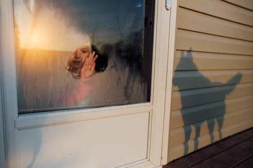 Mädchen wischt den Reif vom Fenster, während der Schatten eines Hundes auf dem Haus erscheint - CAVF89501