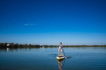 Girl paddleboarding in lake outside of lawrence kansas - CAVF89506
